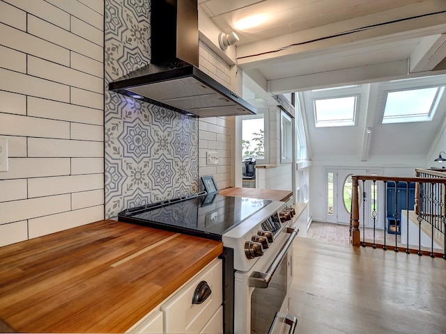 kitchen with stainless steel range, a healthy amount of sunlight, butcher block countertops, and wall chimney exhaust hood