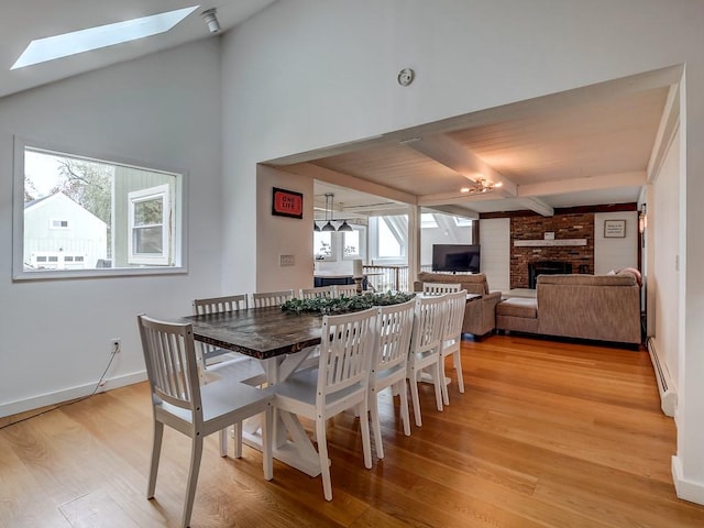 dining area featuring vaulted ceiling with skylight, a fireplace, a baseboard heating unit, and light wood-type flooring