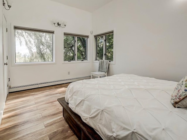 bedroom with light hardwood / wood-style floors and a baseboard heating unit