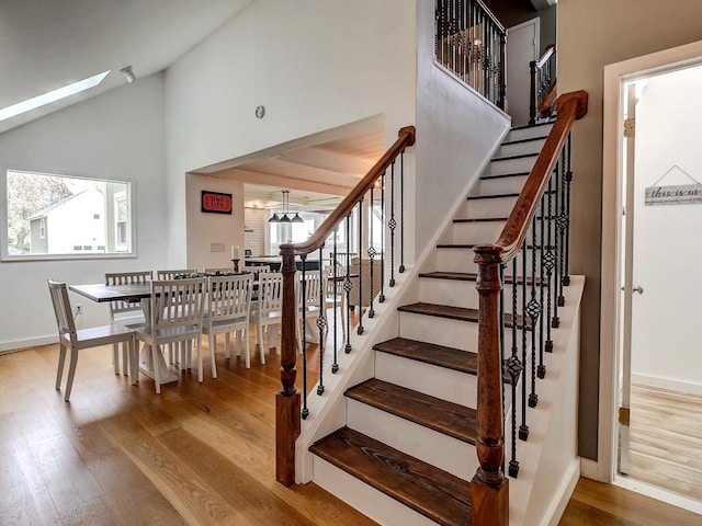 stairs featuring a healthy amount of sunlight, wood-type flooring, high vaulted ceiling, and a skylight