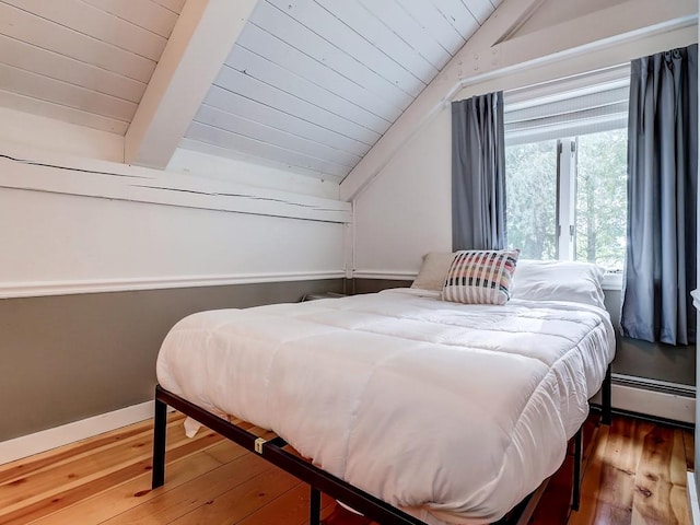 bedroom with lofted ceiling with beams, a baseboard radiator, and hardwood / wood-style flooring