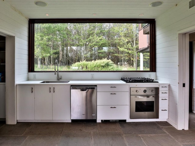 kitchen featuring appliances with stainless steel finishes, wood ceiling, wooden walls, sink, and white cabinets