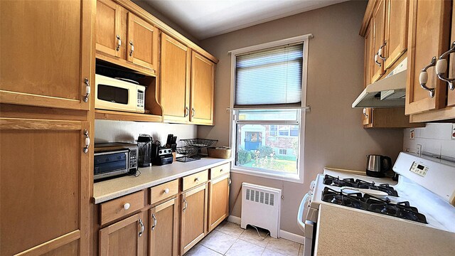 kitchen with white appliances, radiator, under cabinet range hood, and plenty of natural light