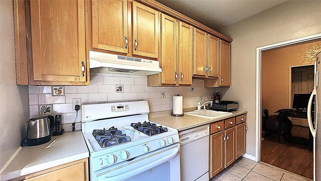 kitchen featuring white appliances, under cabinet range hood, a sink, tasteful backsplash, and light countertops