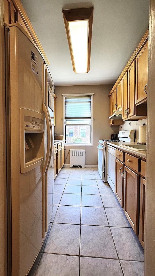 kitchen featuring white appliances, radiator, under cabinet range hood, light tile patterned floors, and light countertops