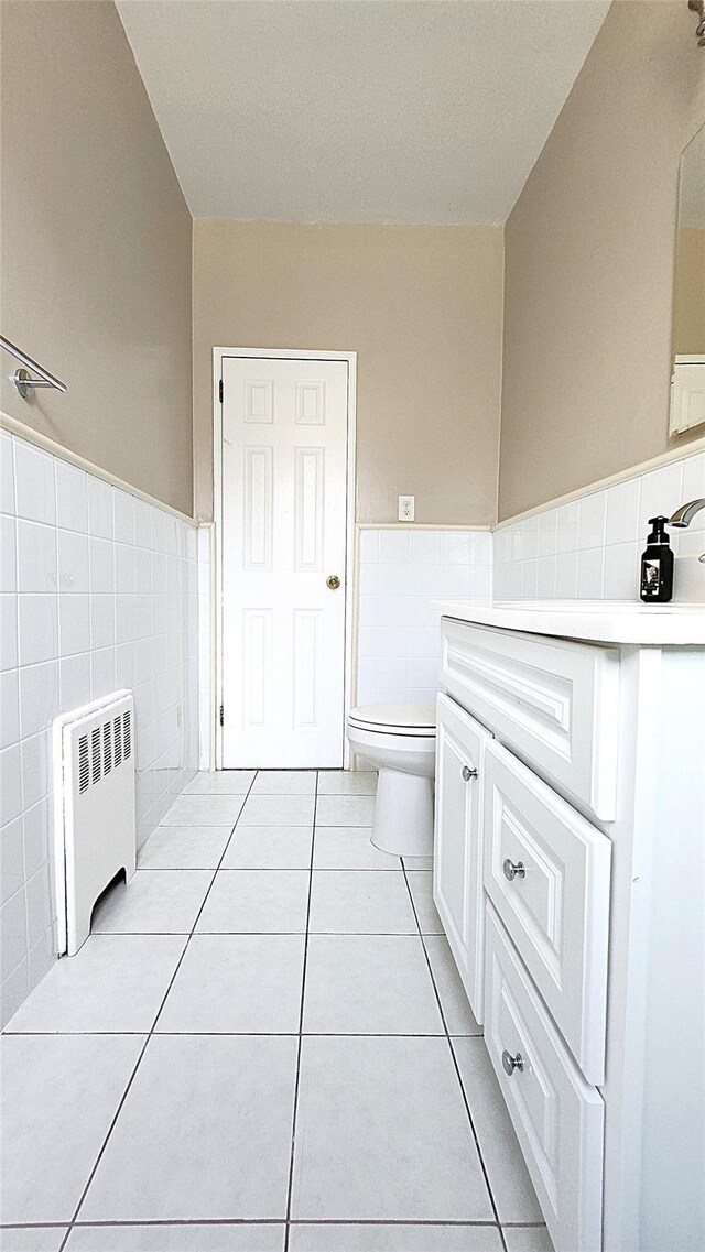 bathroom featuring radiator heating unit, tile walls, vanity, toilet, and tile patterned floors
