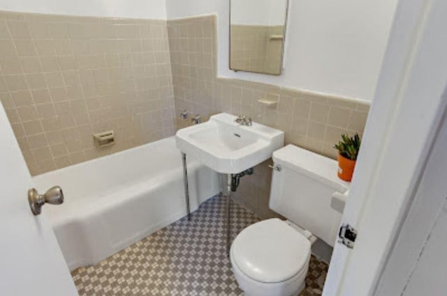 bathroom with tiled shower / bath combo, toilet, and tile walls