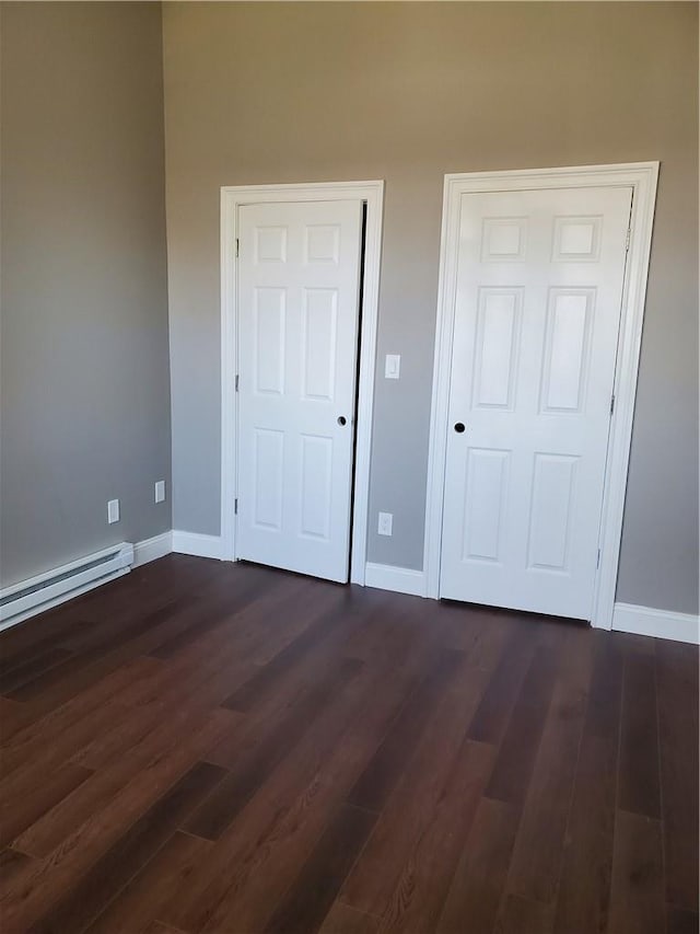 unfurnished bedroom with a baseboard heating unit and dark wood-type flooring