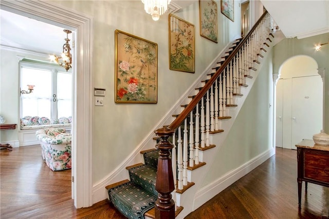 staircase with ornamental molding, a notable chandelier, and hardwood / wood-style flooring