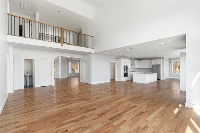201 Tweed Blvd, Piermont, NY 10960 - unfurnished living room featuring a towering ceiling, light wood finished floors, and recessed lighting