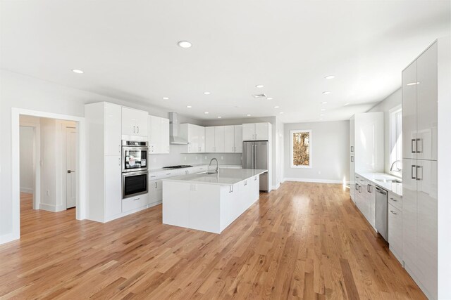 201 Tweed Blvd, Piermont, NY 10960 - kitchen featuring appliances with stainless steel finishes, wall chimney range hood, light countertops, light wood-style flooring, and recessed lighting