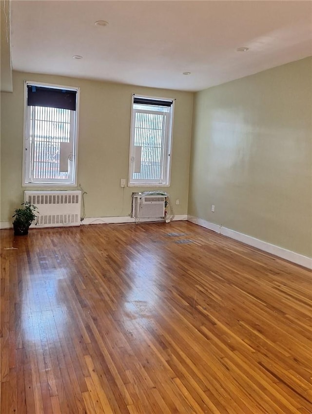 unfurnished room featuring a wall mounted air conditioner, radiator heating unit, and hardwood / wood-style floors