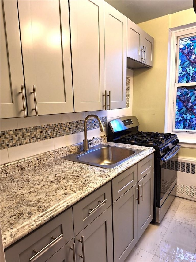 kitchen featuring gray cabinetry, radiator, sink, stainless steel gas stove, and light stone counters