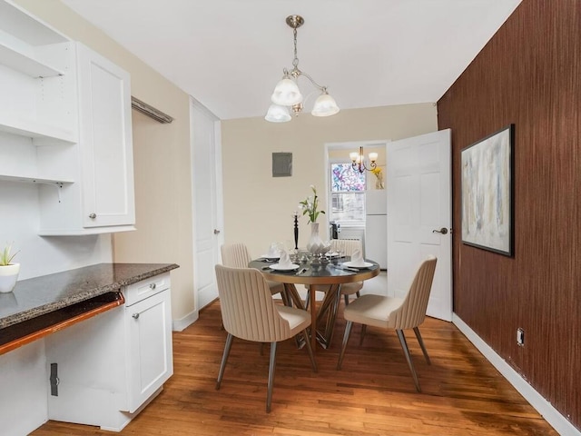 dining room featuring light wood-type flooring, wood walls, baseboards, and a notable chandelier