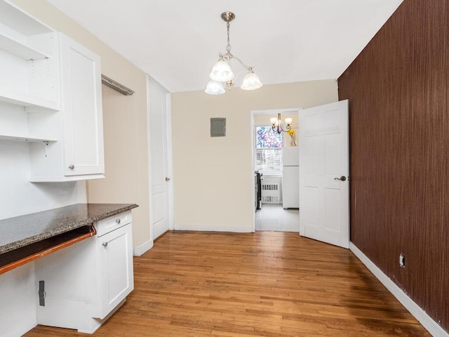 unfurnished dining area featuring light wood-style floors, radiator heating unit, a notable chandelier, and baseboards