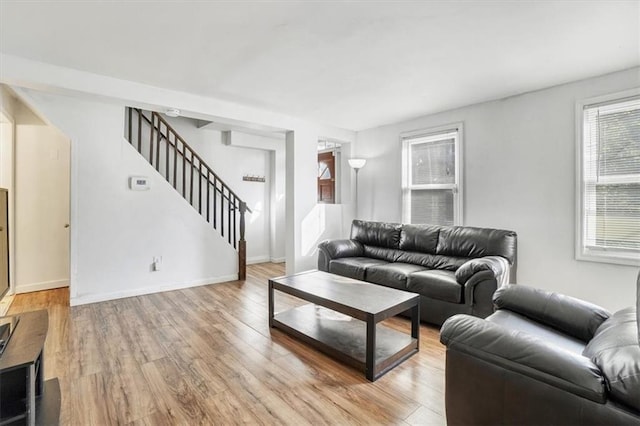 living area featuring stairs, light wood finished floors, and baseboards