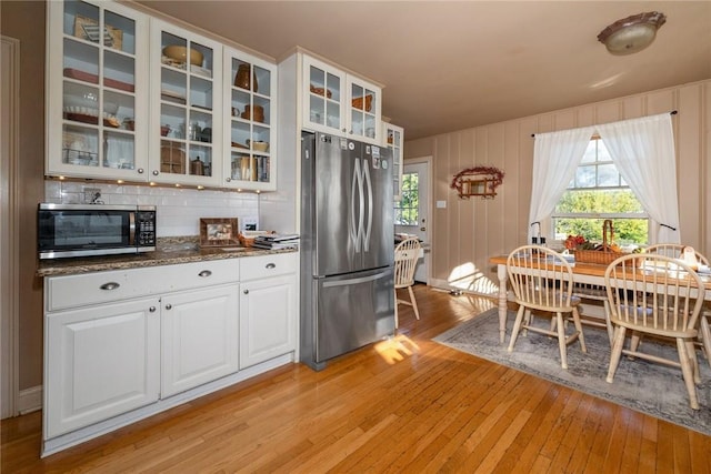 kitchen with white cabinetry, stainless steel appliances, tasteful backsplash, dark stone countertops, and light hardwood / wood-style floors