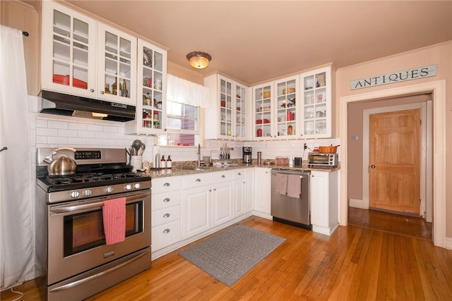 kitchen with stone counters, white cabinets, light hardwood / wood-style flooring, appliances with stainless steel finishes, and tasteful backsplash