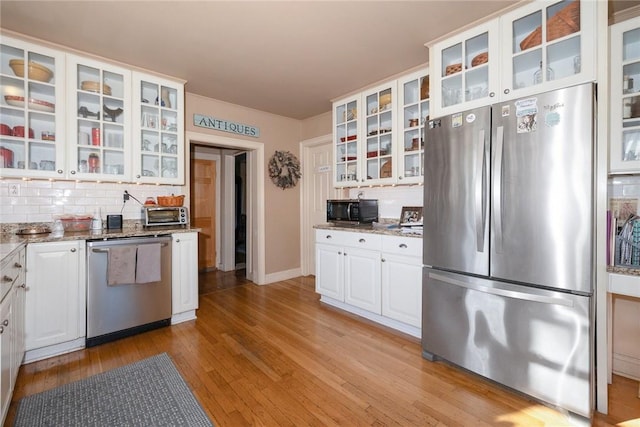 kitchen with backsplash, white cabinets, dark stone countertops, light wood-type flooring, and appliances with stainless steel finishes