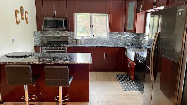 kitchen featuring stainless steel appliances, backsplash, dark stone counters, a breakfast bar, and a kitchen island