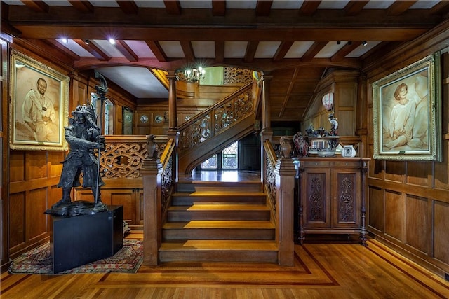 staircase featuring beam ceiling, ornate columns, wooden walls, and wood-type flooring