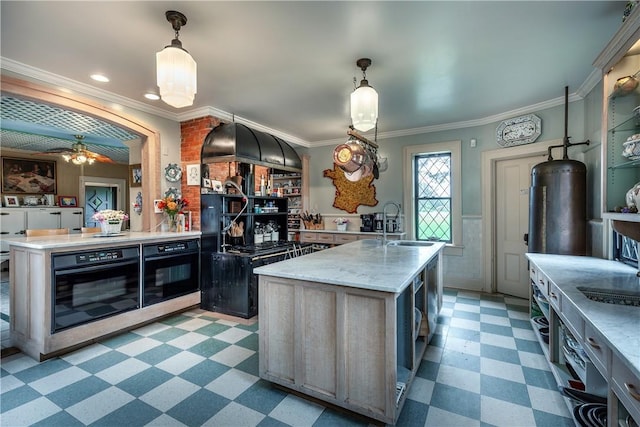 kitchen featuring black oven, an island with sink, decorative light fixtures, and ornamental molding