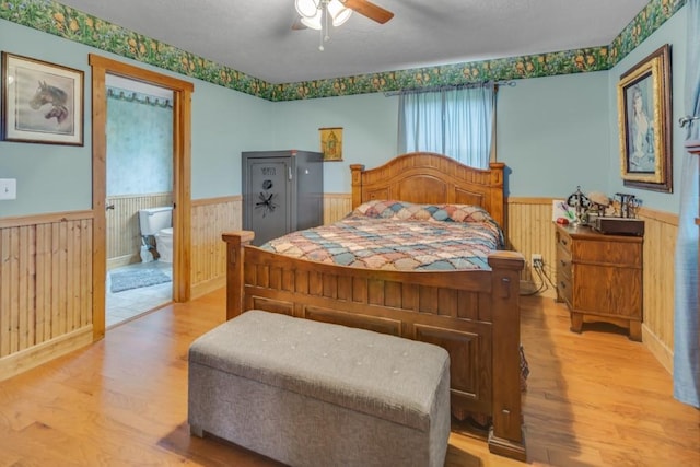 bedroom with ceiling fan, ensuite bathroom, wooden walls, and light hardwood / wood-style flooring