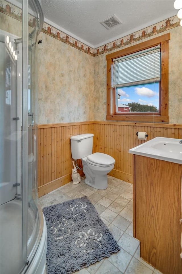 bathroom featuring an enclosed shower, a textured ceiling, vanity, wooden walls, and toilet