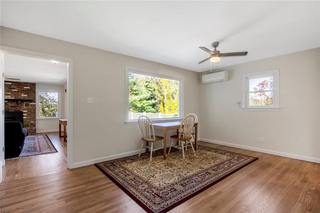 dining space with wood-type flooring, a wall unit AC, ceiling fan, and a brick fireplace