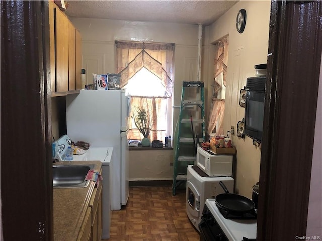 kitchen featuring sink, washer / dryer, dark parquet floors, a textured ceiling, and white appliances