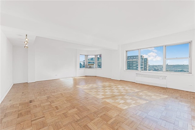 empty room featuring a wealth of natural light, light parquet floors, and radiator