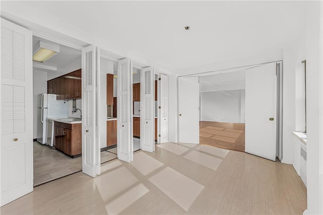 unfurnished bedroom featuring white refrigerator, ensuite bathroom, light hardwood / wood-style flooring, and sink