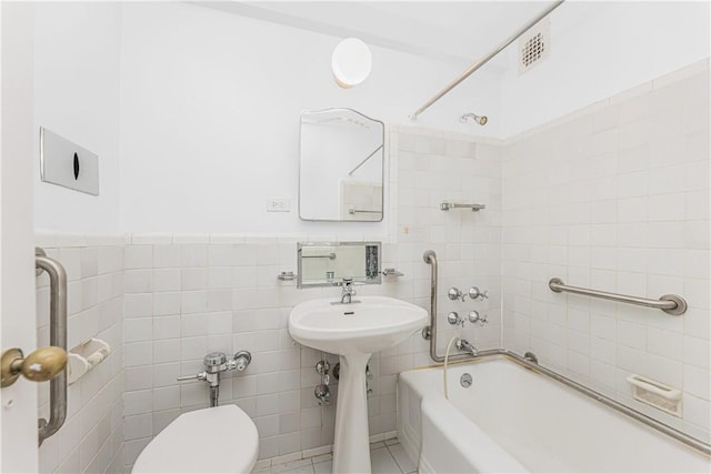 bathroom with tiled shower / bath, toilet, tile walls, and tile patterned floors