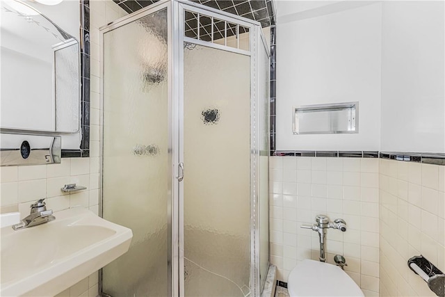 bathroom featuring toilet, a shower with door, sink, and tile walls