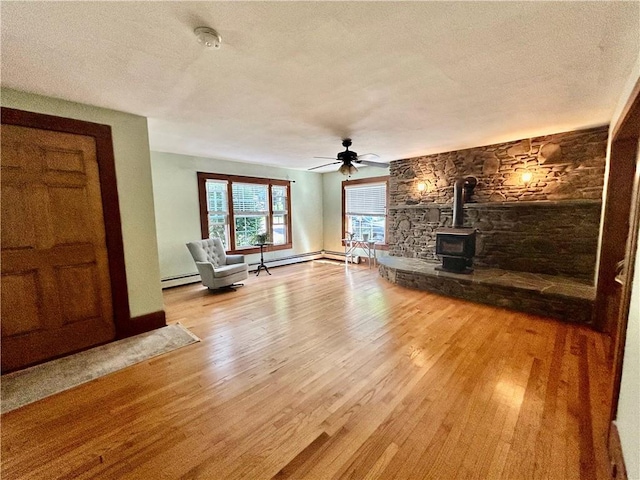 unfurnished living room featuring a textured ceiling, wood-type flooring, baseboard heating, and a wood stove