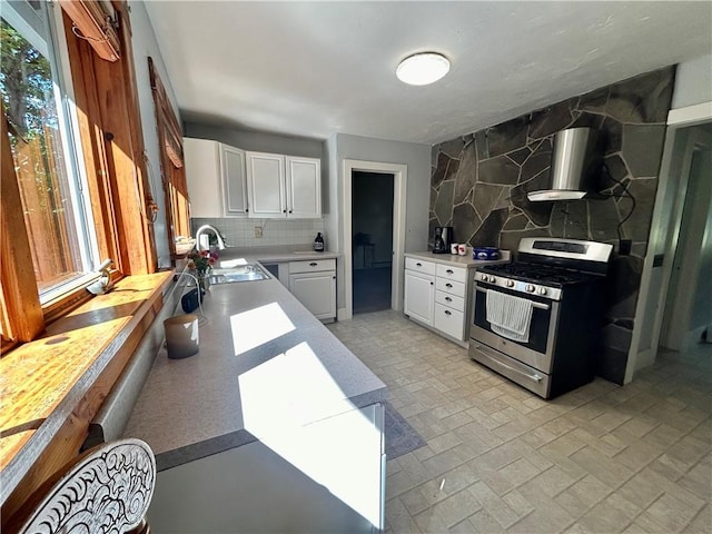 kitchen featuring backsplash, exhaust hood, sink, stainless steel range oven, and white cabinets