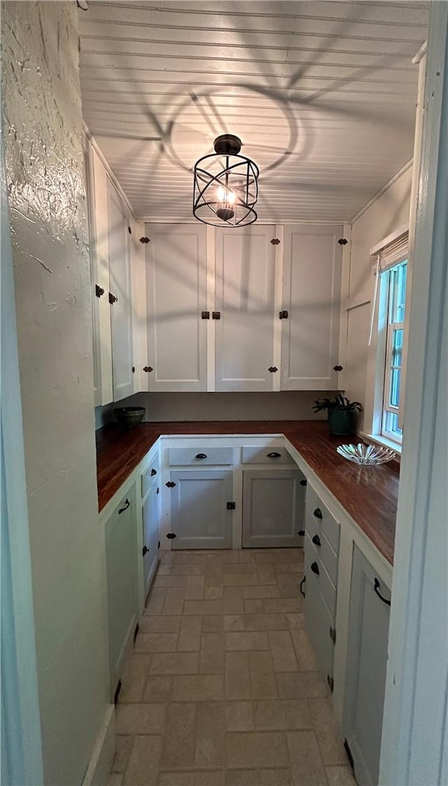 kitchen with wooden counters, pendant lighting, white cabinetry, and a notable chandelier