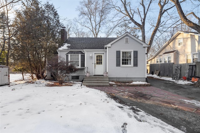 bungalow-style home with entry steps, a shingled roof, a chimney, and fence