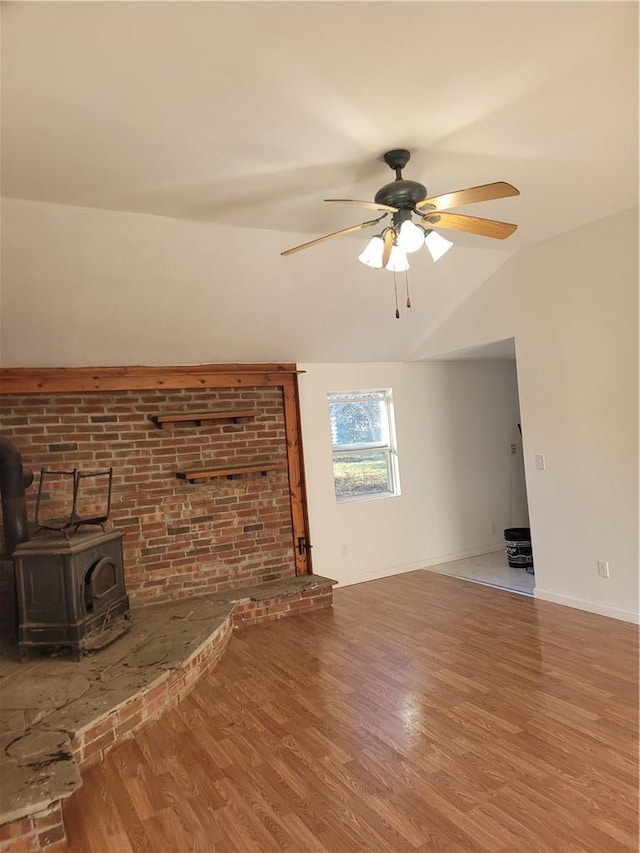 unfurnished living room with baseboards, a ceiling fan, wood finished floors, a wood stove, and vaulted ceiling