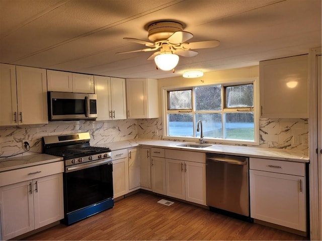 kitchen featuring stainless steel appliances, backsplash, white cabinetry, a sink, and wood finished floors