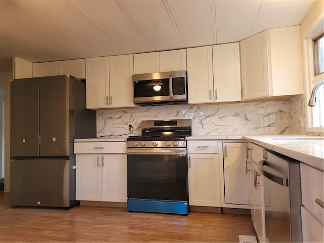 kitchen with white cabinets, appliances with stainless steel finishes, light countertops, light wood-type flooring, and a sink