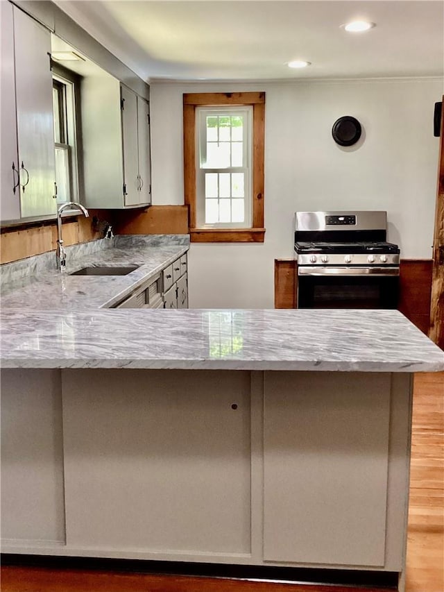 kitchen featuring kitchen peninsula, light wood-type flooring, light stone counters, sink, and stainless steel range with gas cooktop