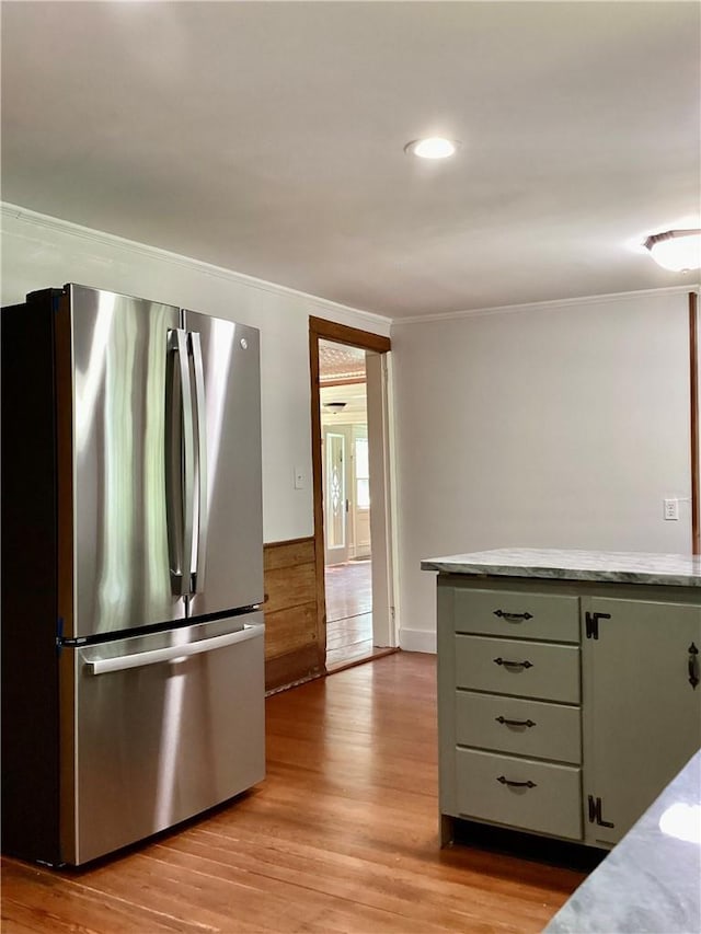 kitchen with green cabinets, light hardwood / wood-style flooring, light stone countertops, ornamental molding, and stainless steel refrigerator