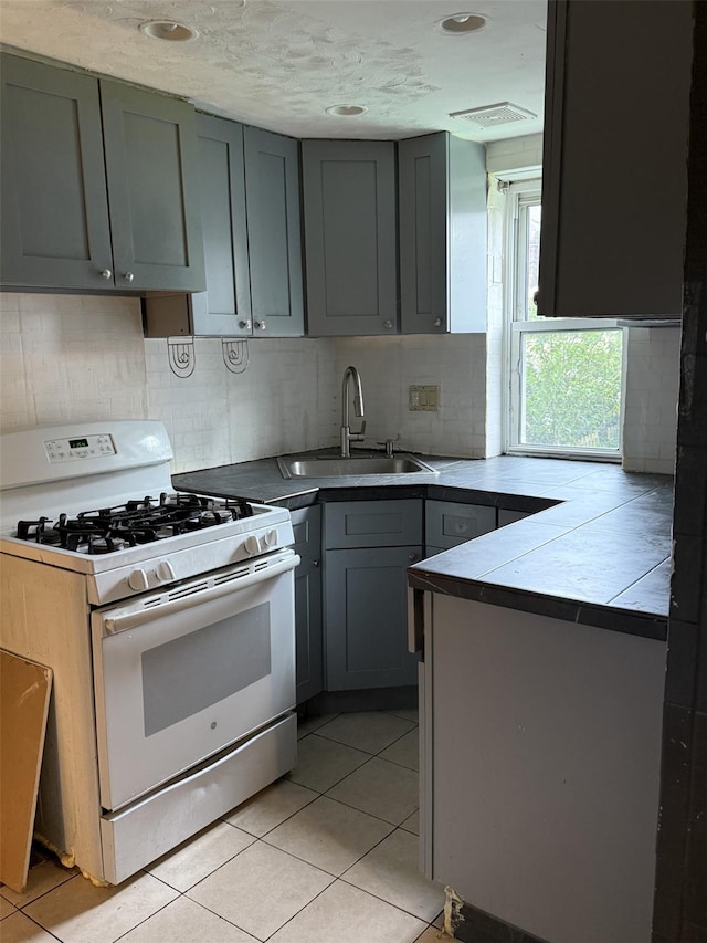 1246 Troy Ave, Brooklyn, NY 11203 - kitchen with white range with gas stovetop, a sink, tile counters, gray cabinets, and tasteful backsplash