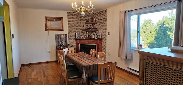 dining area featuring a large fireplace, a notable chandelier, a baseboard heating unit, wood-type flooring, and ornamental molding