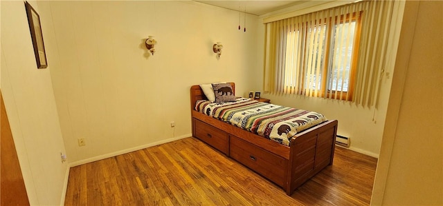 bedroom with wood-type flooring and a baseboard heating unit