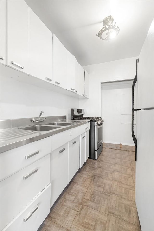 kitchen featuring white cabinetry, stainless steel gas stove, sink, white refrigerator, and light parquet flooring