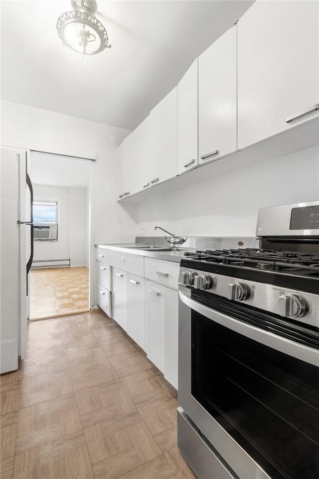 kitchen with sink, a baseboard radiator, stainless steel gas range oven, white fridge, and white cabinets