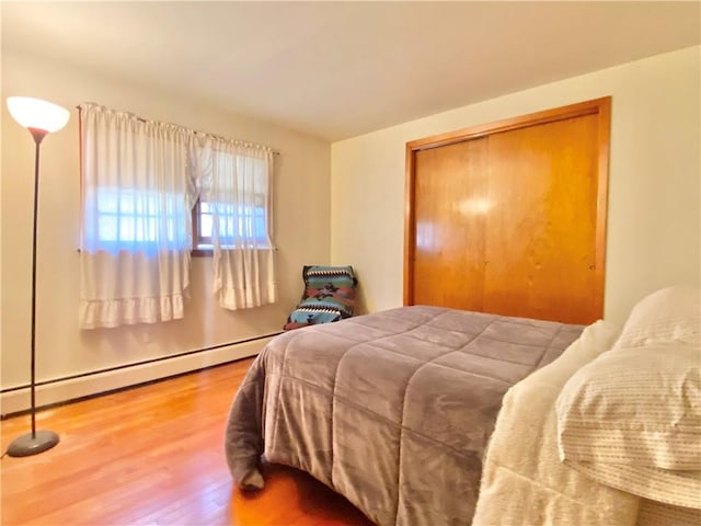 bedroom with hardwood / wood-style flooring, baseboard heating, and a closet