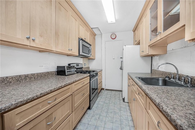 kitchen with light brown cabinetry, stainless steel appliances, light stone counters, and sink